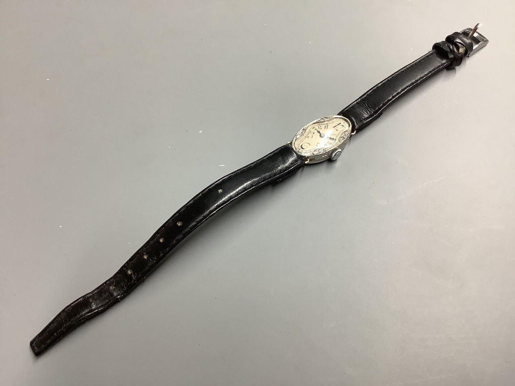 A lady’s mid 20th century white metal stamped platine and diamond set oval cocktail watch, on a leather strap.